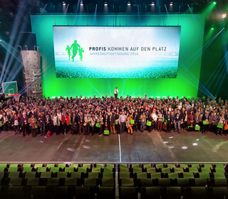 Gruppenbild aller anwesenden Mitarbeiter vor großer Leinwand mit Veranstaltungslogo